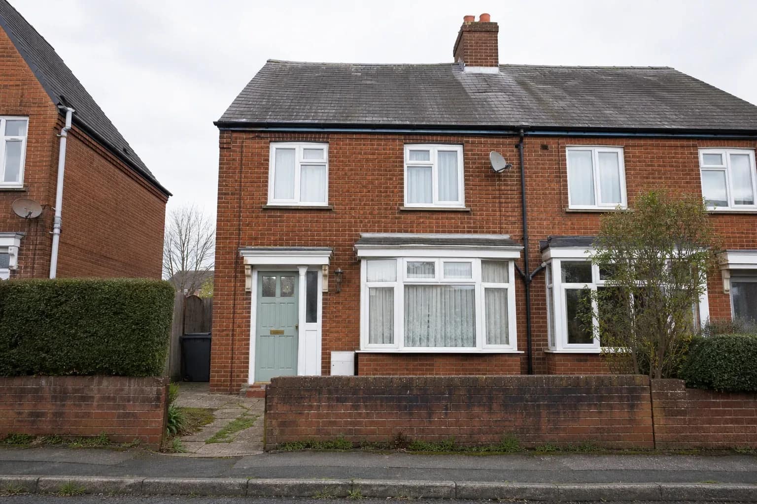 Two-storey brick house photographed square-on from the opposite pavement on an overcast morning