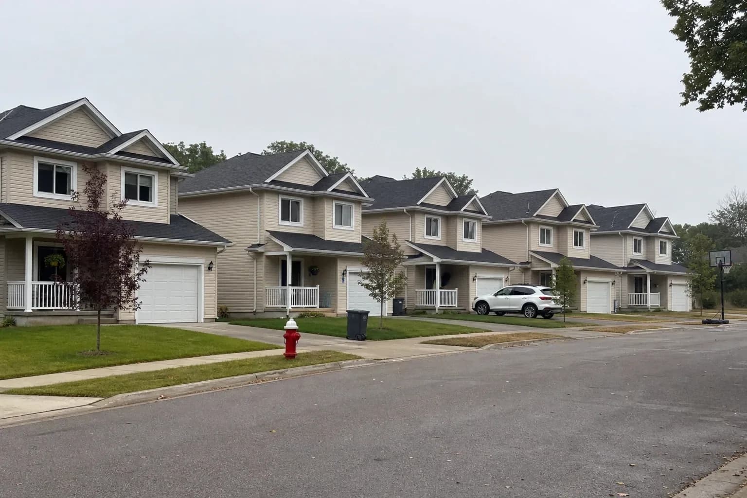 Row of similar detached houses with matching rooflines and porches along a quiet suburban street