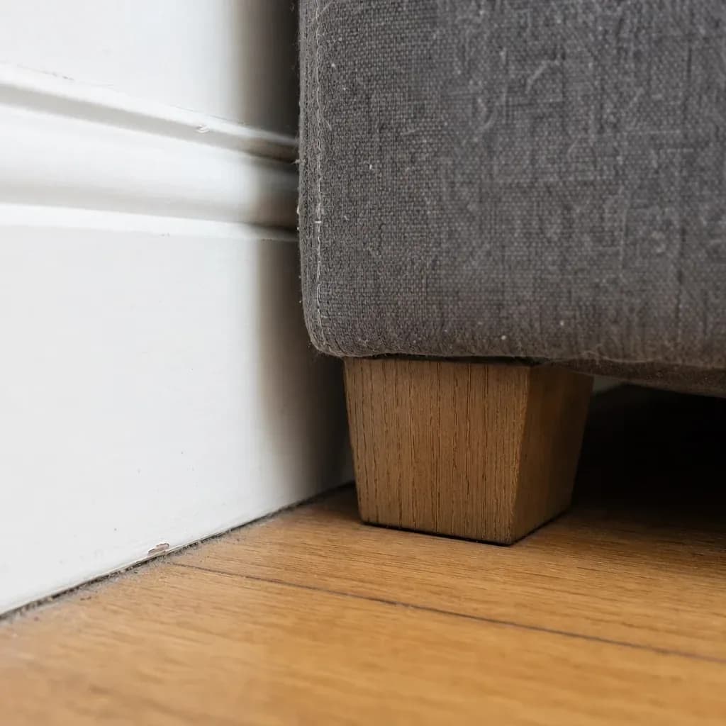 Close detail of a grey sofa leg meeting a painted skirting board with a soft shadow on the floor