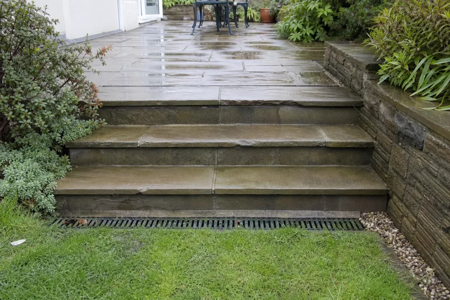 Stone garden steps after rain with a channel drain running along the base of the top step