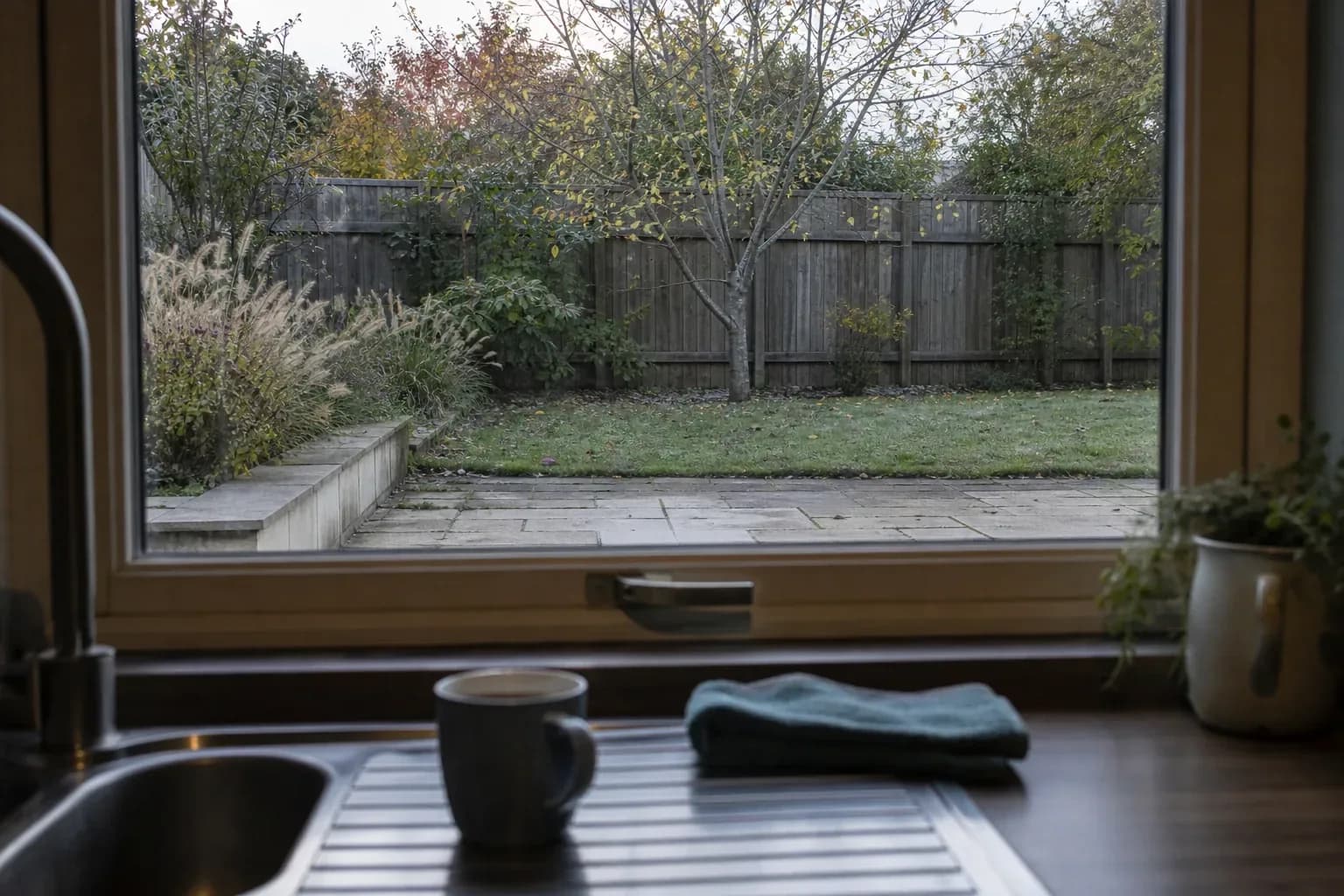 Looking out through a kitchen window over the sink to a paved terrace and border beyond