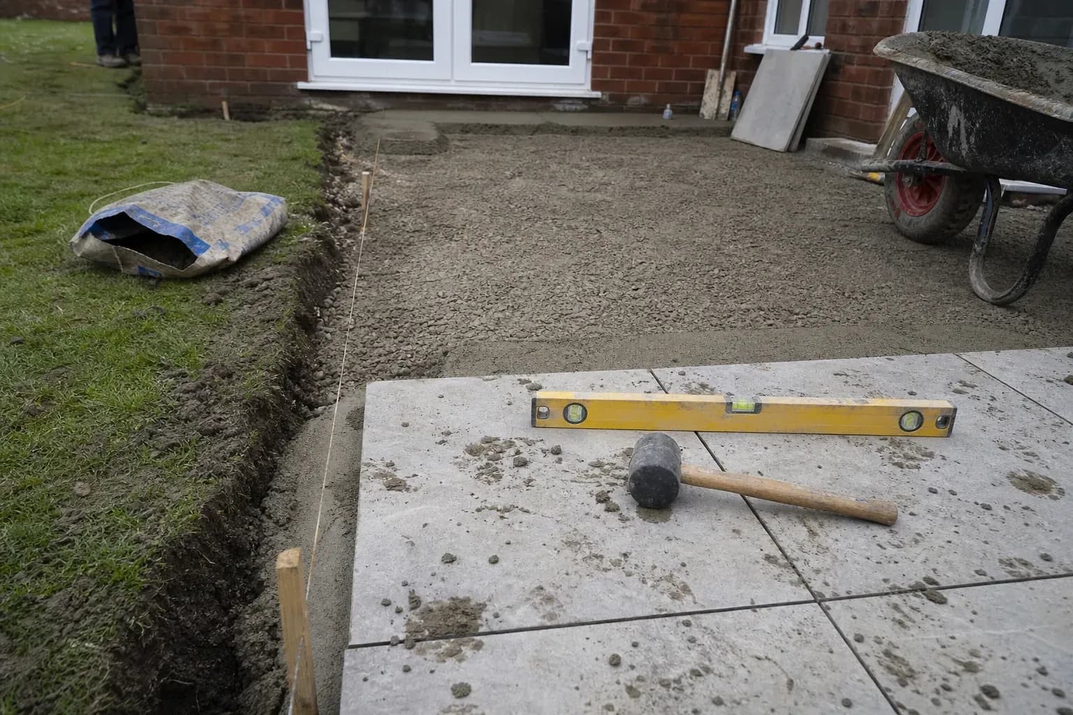 Patio mid-build with compacted sub-base, a taut string line and the first slabs laid at the corner