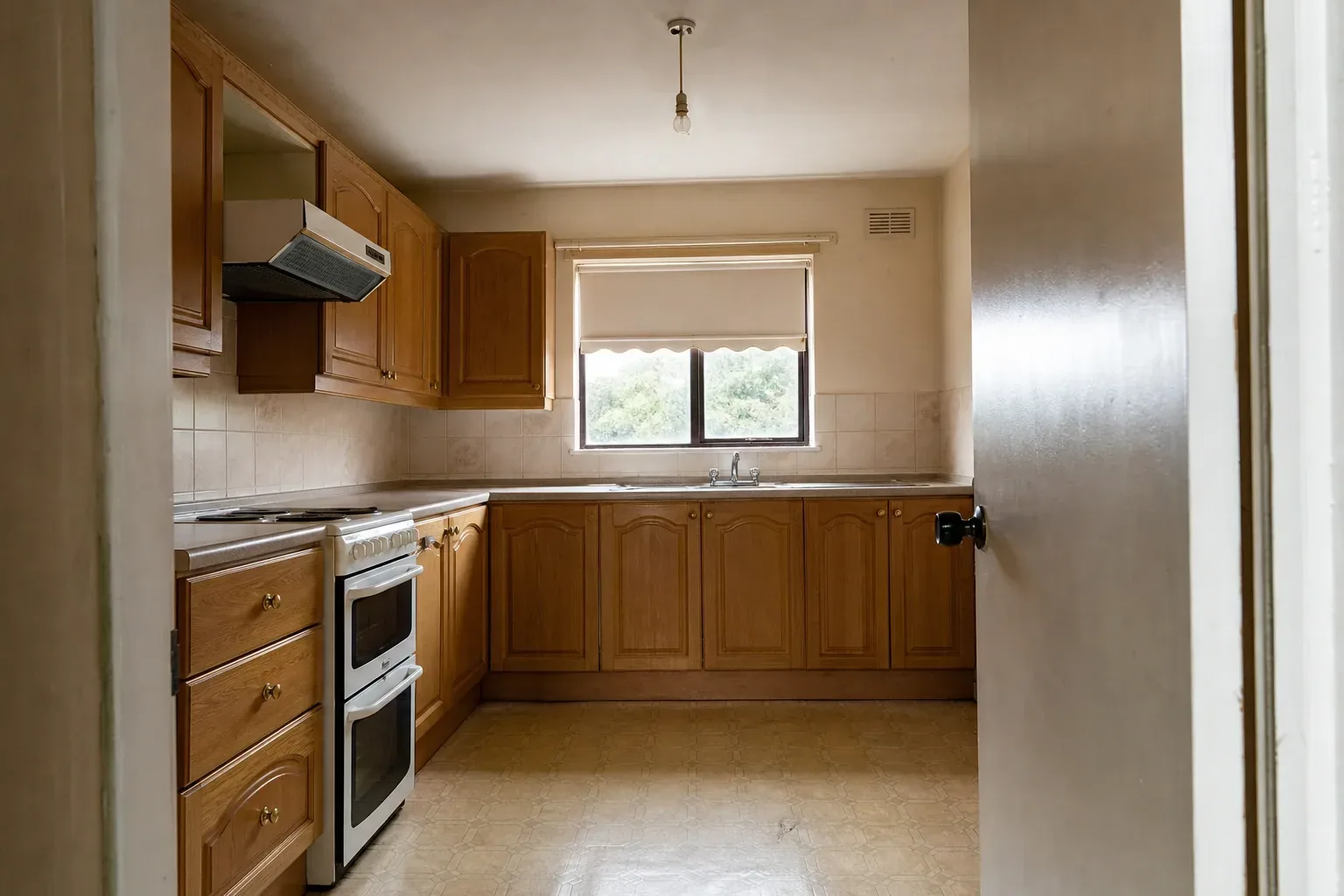 Dated kitchen with honey oak cabinets, laminate worktop and worn beige vinyl flooring