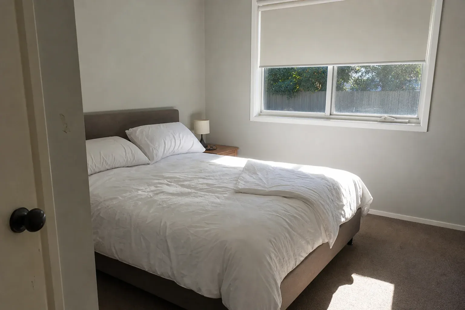 Morning light falls across rumpled white bedding in a plain bedroom shot from the doorway