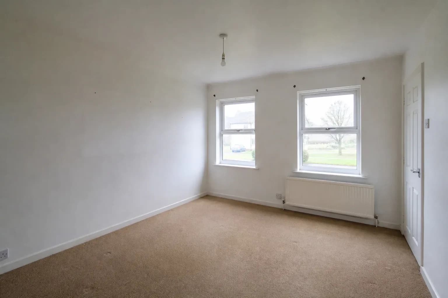 An empty carpeted living room shot from the corner, showing marks where furniture once stood